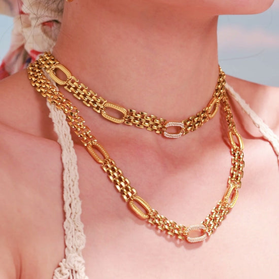 Model wearing layered gold-tone chain necklaces with oval links and matching hoop earrings.