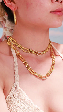 Model wearing layered gold-tone chain necklaces with oval links and matching hoop earrings.