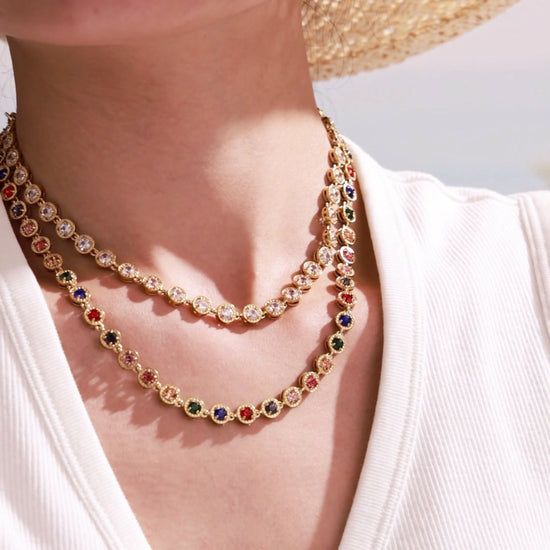 Model wearing layered gold-tone tennis necklaces and matching drop earrings with clear and multicolor round crystal settings for wholesale jewelry collections.