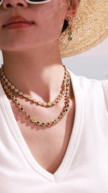 Model wearing layered gold-tone tennis necklaces and matching drop earrings with clear and multicolor round crystal settings for wholesale jewelry collections.