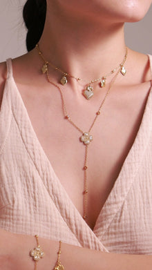 Layered gold-tone necklaces featuring heart charms and a clear-stone clover lariat, with matching bracelets on a model.