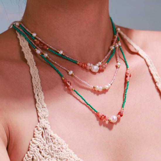 Model wearing layered green and pink beaded necklaces with white pearl accents and gold-tone spacer beads.