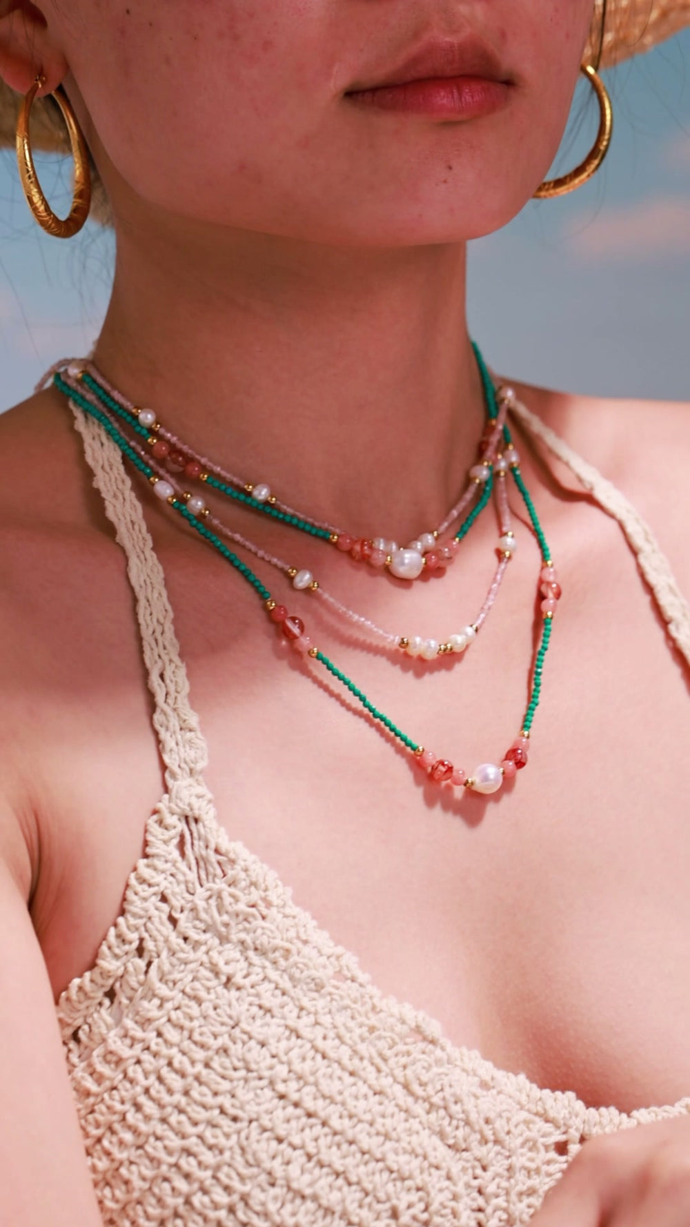 Model wearing layered green and pink beaded necklaces with white pearl accents and gold-tone spacer beads.