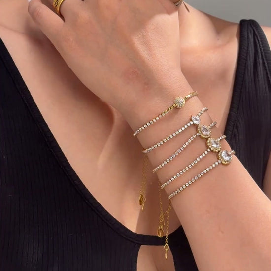 Gold-tone jewelry with rows of clear sparkling stones and decorative center accents shown as necklaces and stacked bracelets on a model