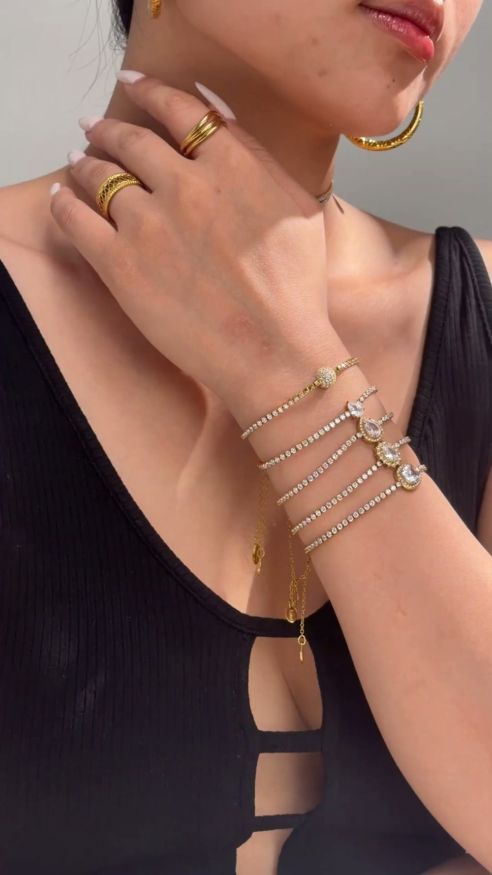Gold-tone jewelry with rows of clear sparkling stones and decorative center accents shown as necklaces and stacked bracelets on a model