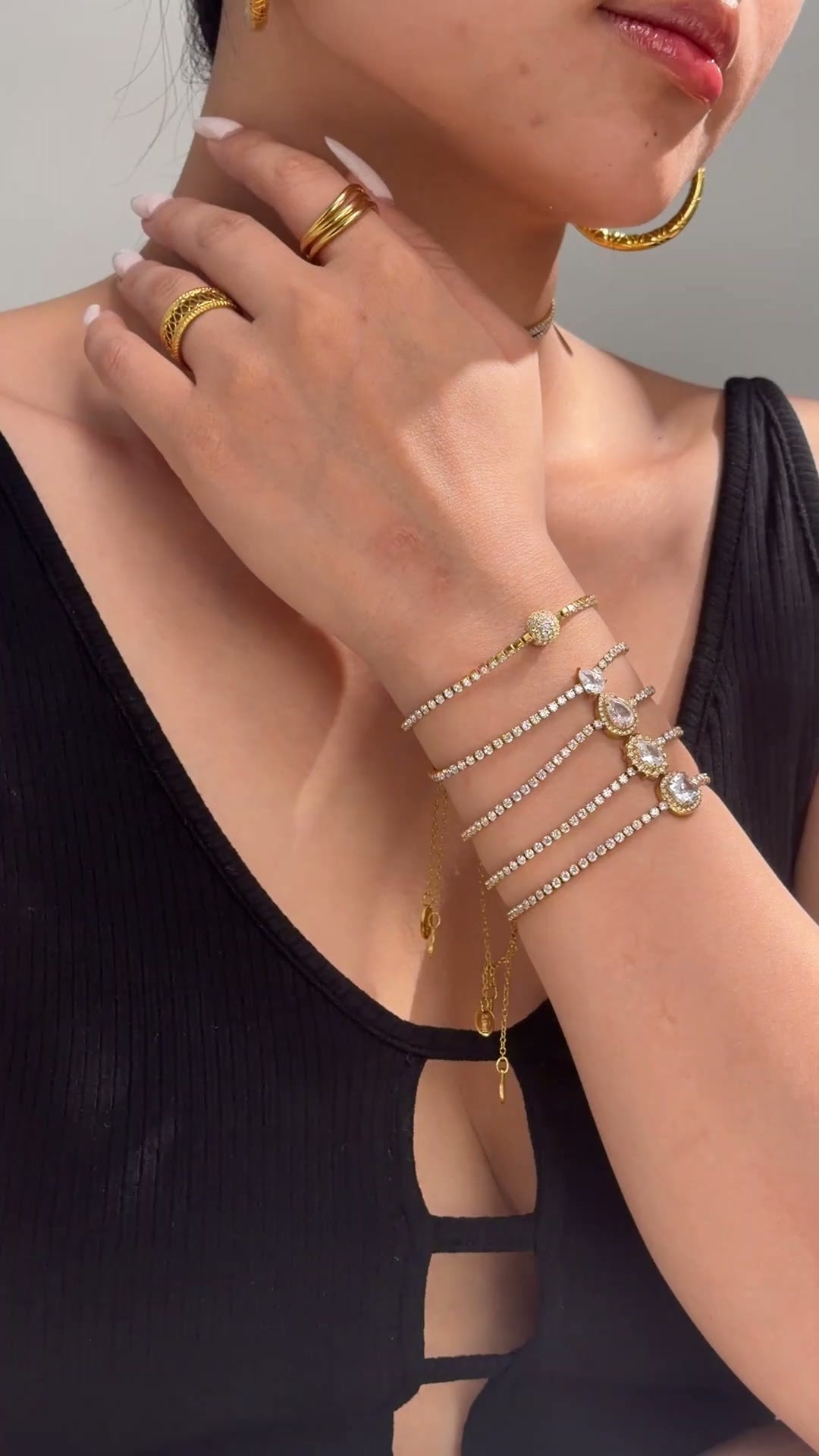 Gold-tone jewelry with rows of clear sparkling stones and decorative center accents shown as necklaces and stacked bracelets on a model
