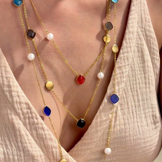 Layered gold-tone station necklaces with colorful rounded-square stones, white pearl-like beads and gold-tone discs, shown on a model.