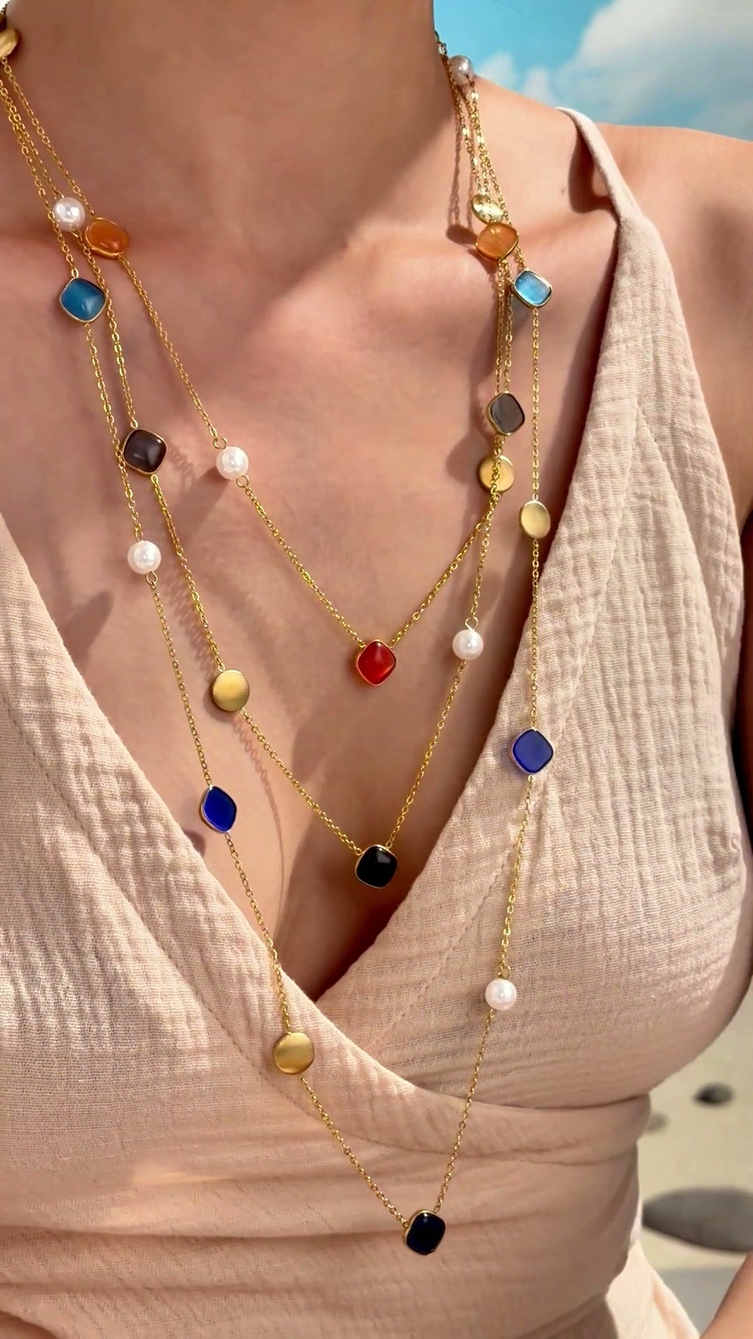 Layered gold-tone station necklaces with colorful rounded-square stones, white pearl-like beads and gold-tone discs, shown on a model.