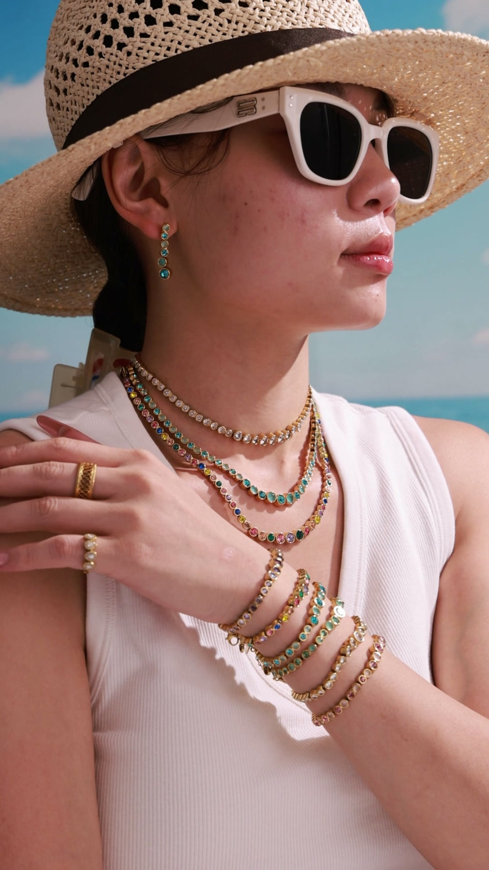 Model wearing layered gold-tone necklaces, bracelets and drop earrings with colorful round crystal details for wholesale jewelry collections.