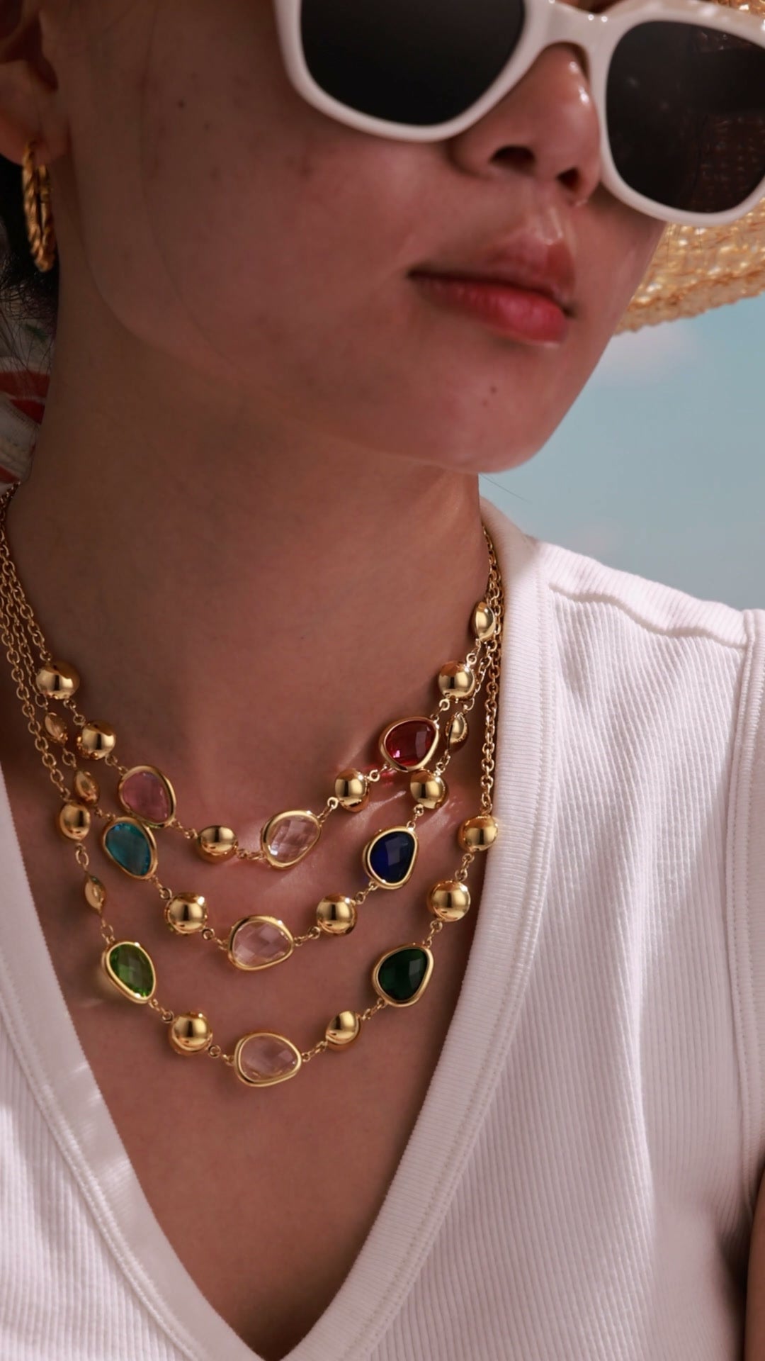 Model wearing layered gold-tone necklaces with colorful faceted stones and polished gold-tone beads.