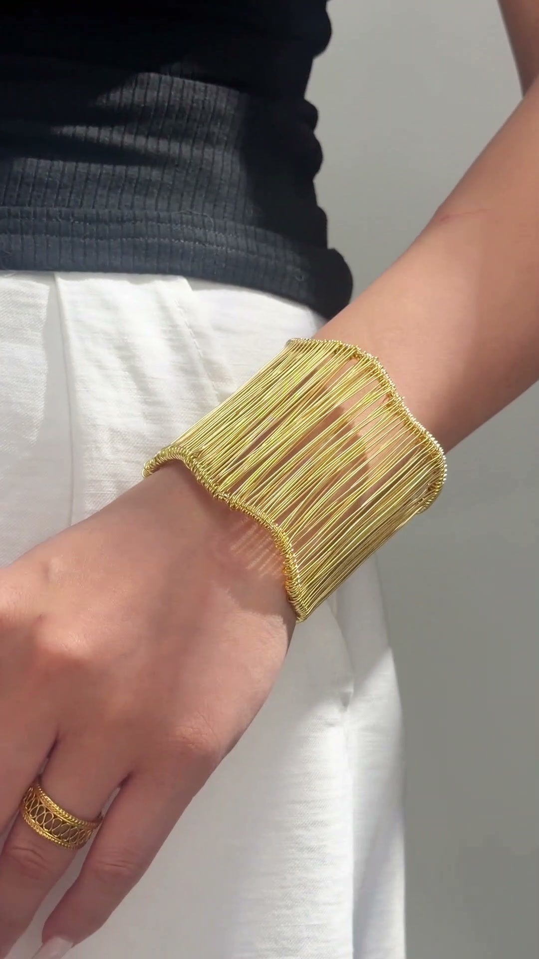 Wide gold-tone openwork cuff bracelet with fine vertical bars and gently curved edges shown on the wrist.