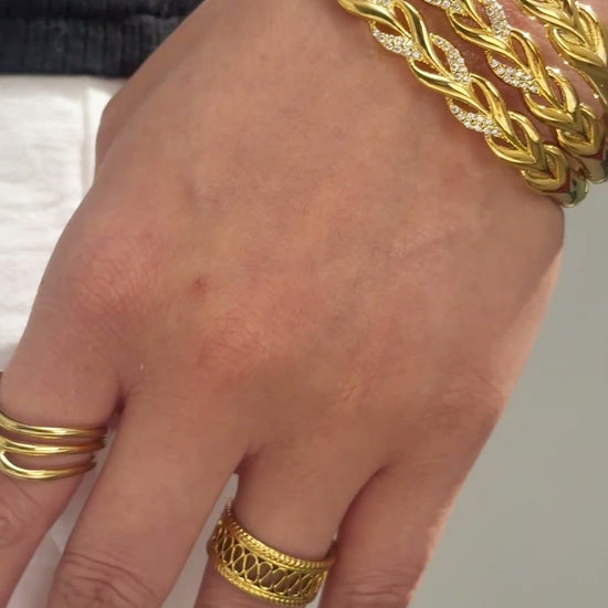 Wide gold-tone openwork cuff bracelet with interwoven leaf-shaped links shown on the wrist.