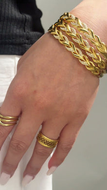 Wide gold-tone openwork cuff bracelet with interwoven leaf-shaped links shown on the wrist.