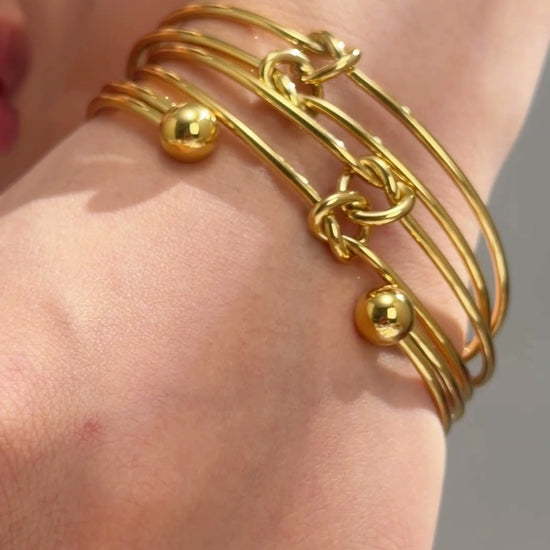 Gold-tone layered wire cuff bracelet with knot details and polished ball ends shown on the wrist.