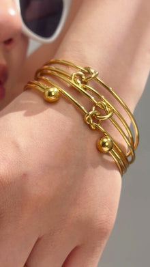 Gold-tone layered wire cuff bracelet with knot details and polished ball ends shown on the wrist.
