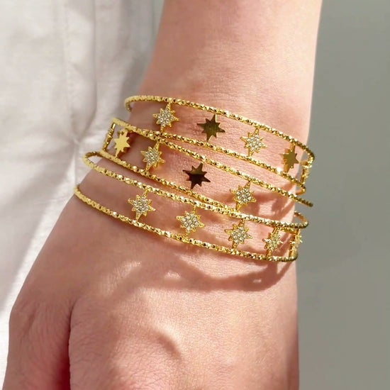 Gold-tone multi-row cuff bracelet with starburst details and textured bands shown on the wrist.