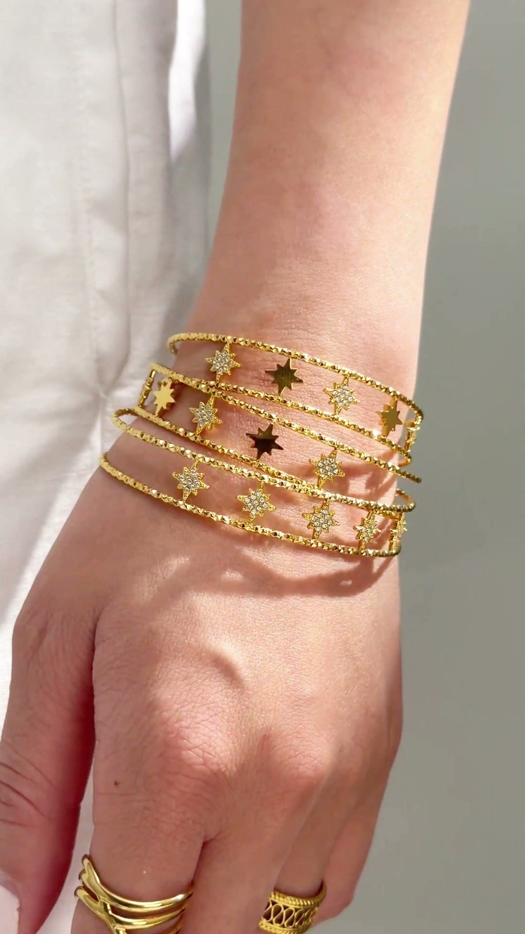 Gold-tone multi-row cuff bracelet with starburst details and textured bands shown on the wrist.