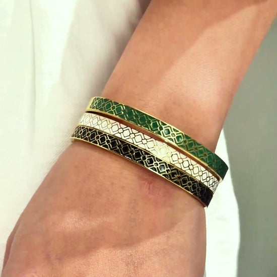 Slim gold-tone bangles with green, white and dark patterned bands shown stacked on the wrist.