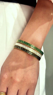 Slim gold-tone bangles with green, white and dark patterned bands shown stacked on the wrist.