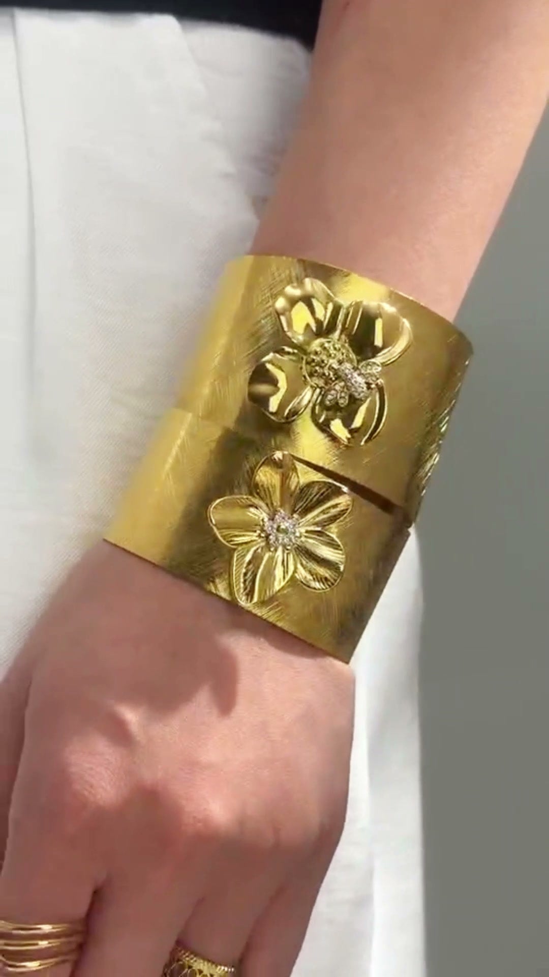 Wide gold-tone cuff bracelets with raised floral details shown stacked on the wrists.