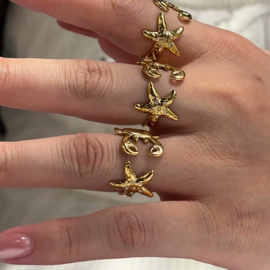 Gold-tone ocean-inspired open rings with zircon starfish and crab details, shown on hand