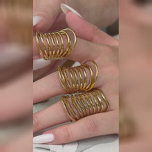 Three wide gold-tone openwork rings with multiple curved bands, shown on a hand with a white manicure.