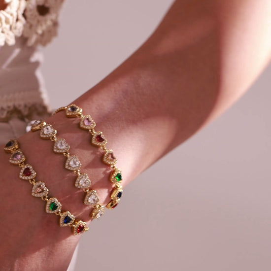 Gold-tone heart-link bracelets with clear and multicolor crystal accents worn by a model
