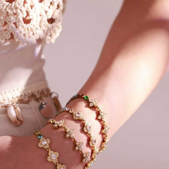 Gold-tone floral bracelets with clear crystal details and colorful accents worn by a model