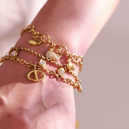 Layered gold-tone charm bracelets with heart and crystal accents worn by a model