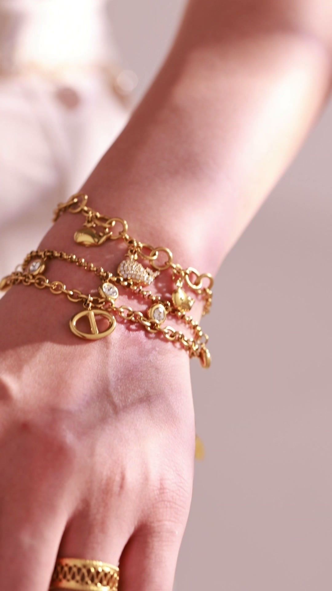 Layered gold-tone charm bracelets with heart and crystal accents worn by a model