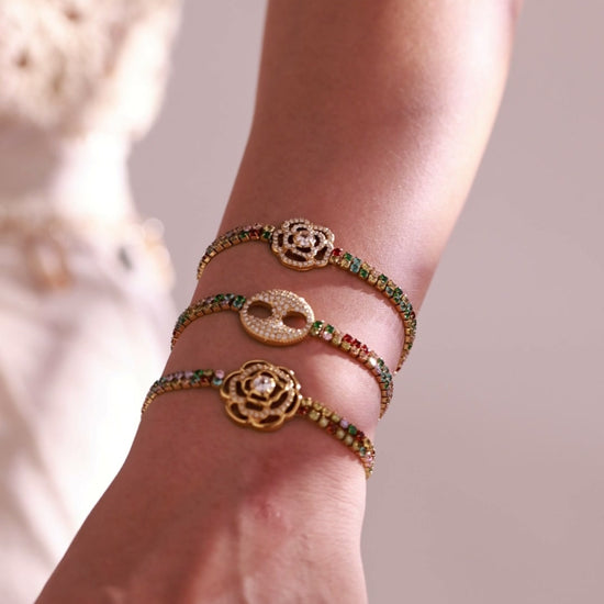 Gold-tone multicolor tennis bracelets with rose and double-ring crystal centerpieces worn by a model