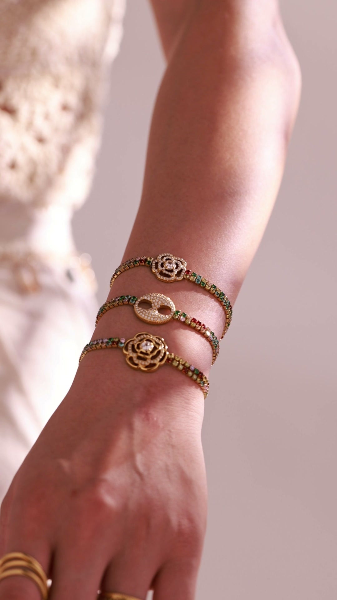 Gold-tone multicolor tennis bracelets with rose and double-ring crystal centerpieces worn by a model
