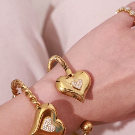 Gold-tone heart cuff bracelets with sparkling pavé heart details, shown on the wrist