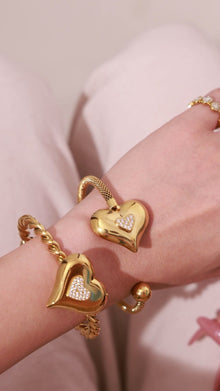 Gold-tone heart cuff bracelets with sparkling pavé heart details, shown on the wrist