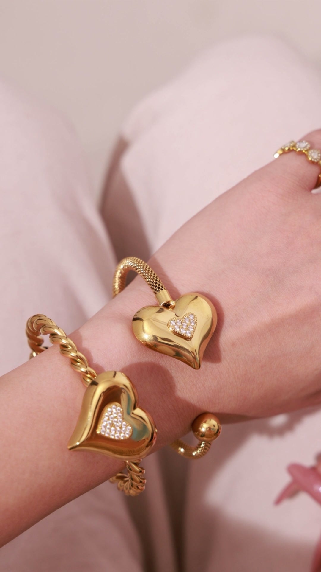 Gold-tone heart cuff bracelets with sparkling pavé heart details, shown on the wrist