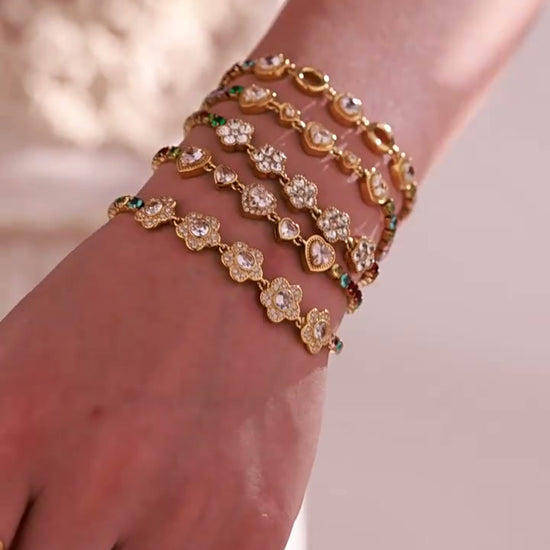 Model wearing layered gold-tone bracelets with floral and multicolor crystal details.