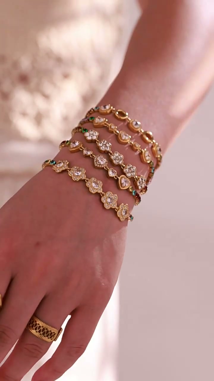 Model wearing layered gold-tone bracelets with floral and multicolor crystal details.