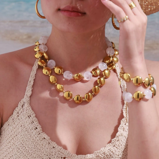 Gold-tone statement necklace with translucent bead details, matching bracelet and hoop earrings shown on a beach model