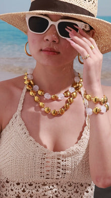 Gold-tone statement necklace with translucent bead details, matching bracelet and hoop earrings shown on a beach model