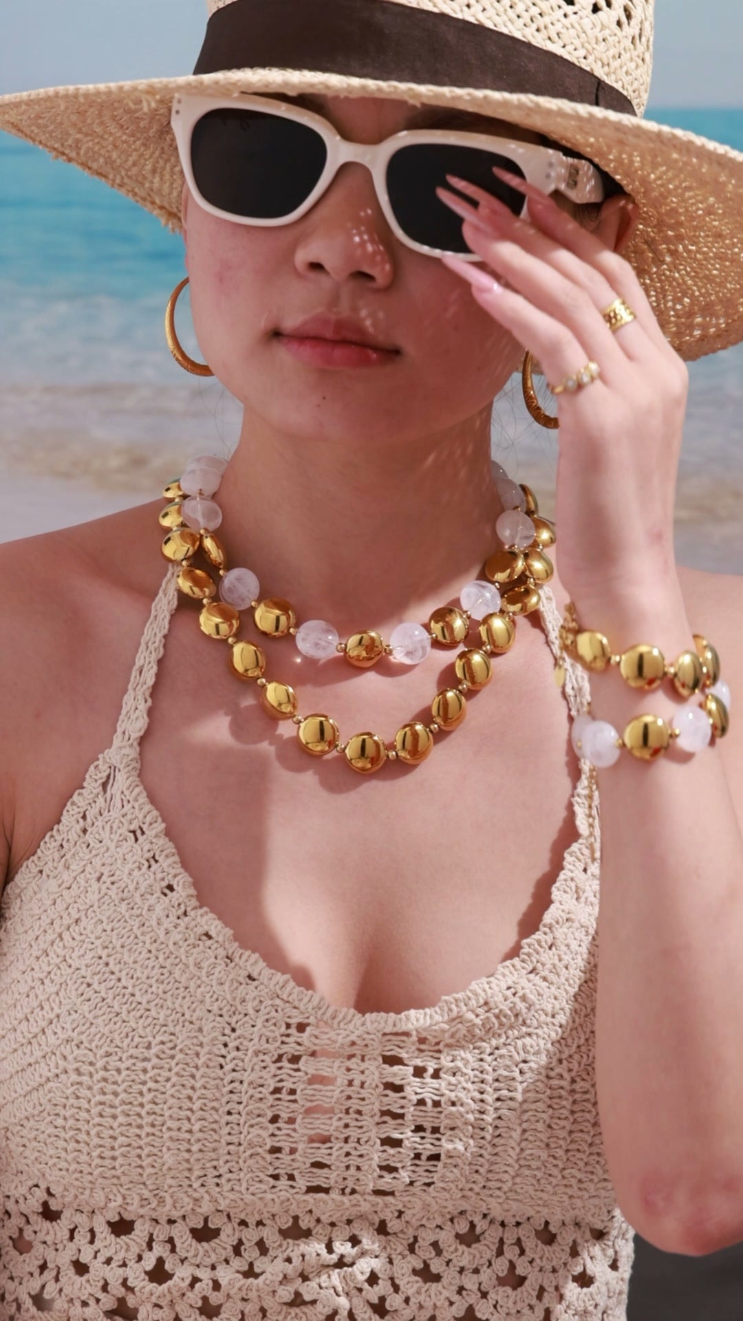 Gold-tone statement necklace with translucent bead details, matching bracelet and hoop earrings shown on a beach model