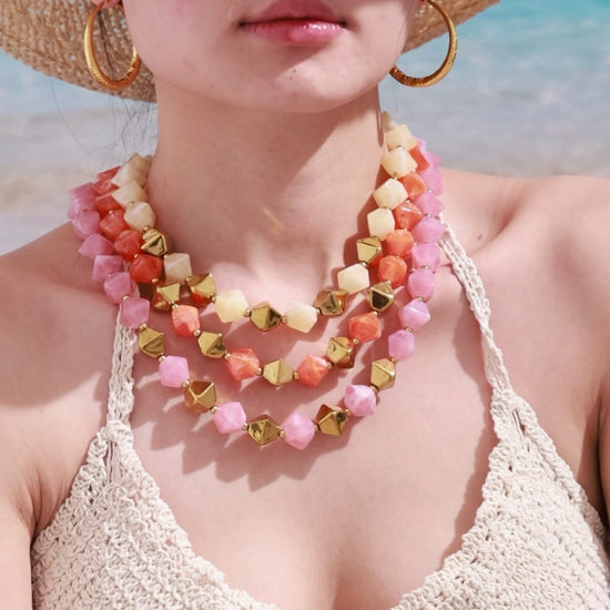 Layered pink, coral and cream faceted bead necklaces with gold-tone geometric beads, shown on a beach model