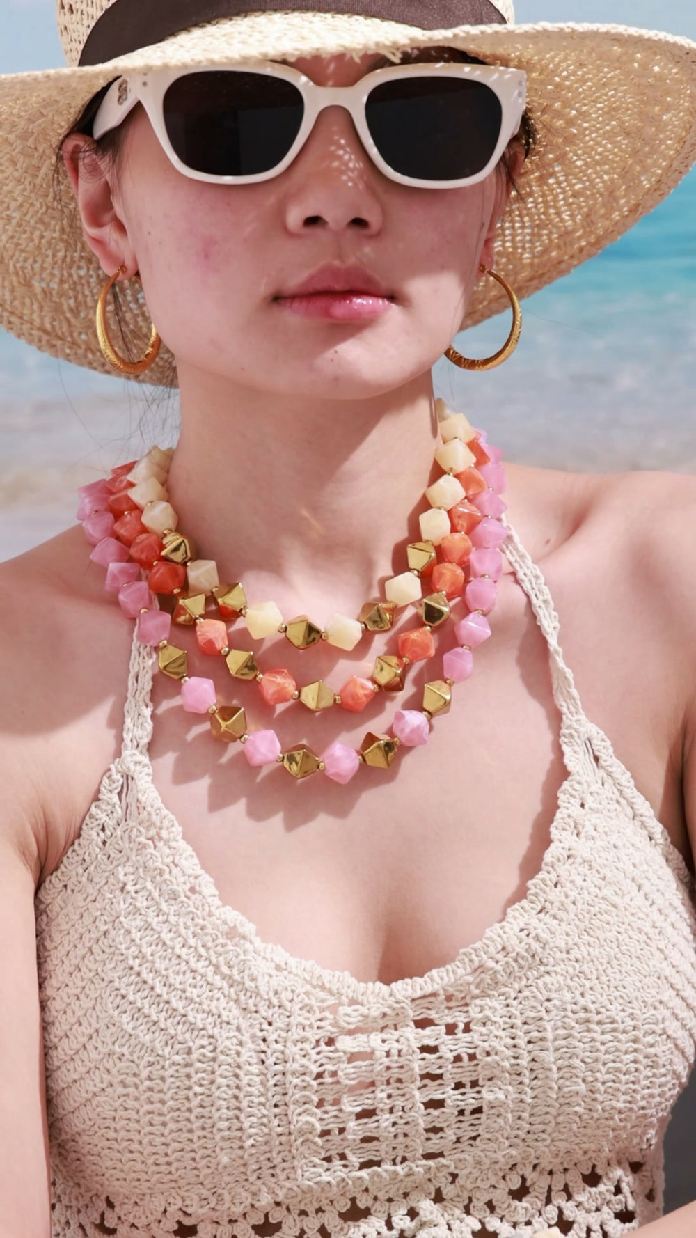 Layered pink, coral and cream faceted bead necklaces with gold-tone geometric beads, shown on a beach model