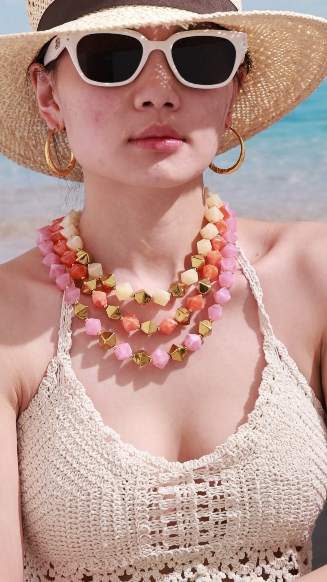 Layered pink, coral and cream faceted bead necklaces with gold-tone geometric beads, shown on a beach model