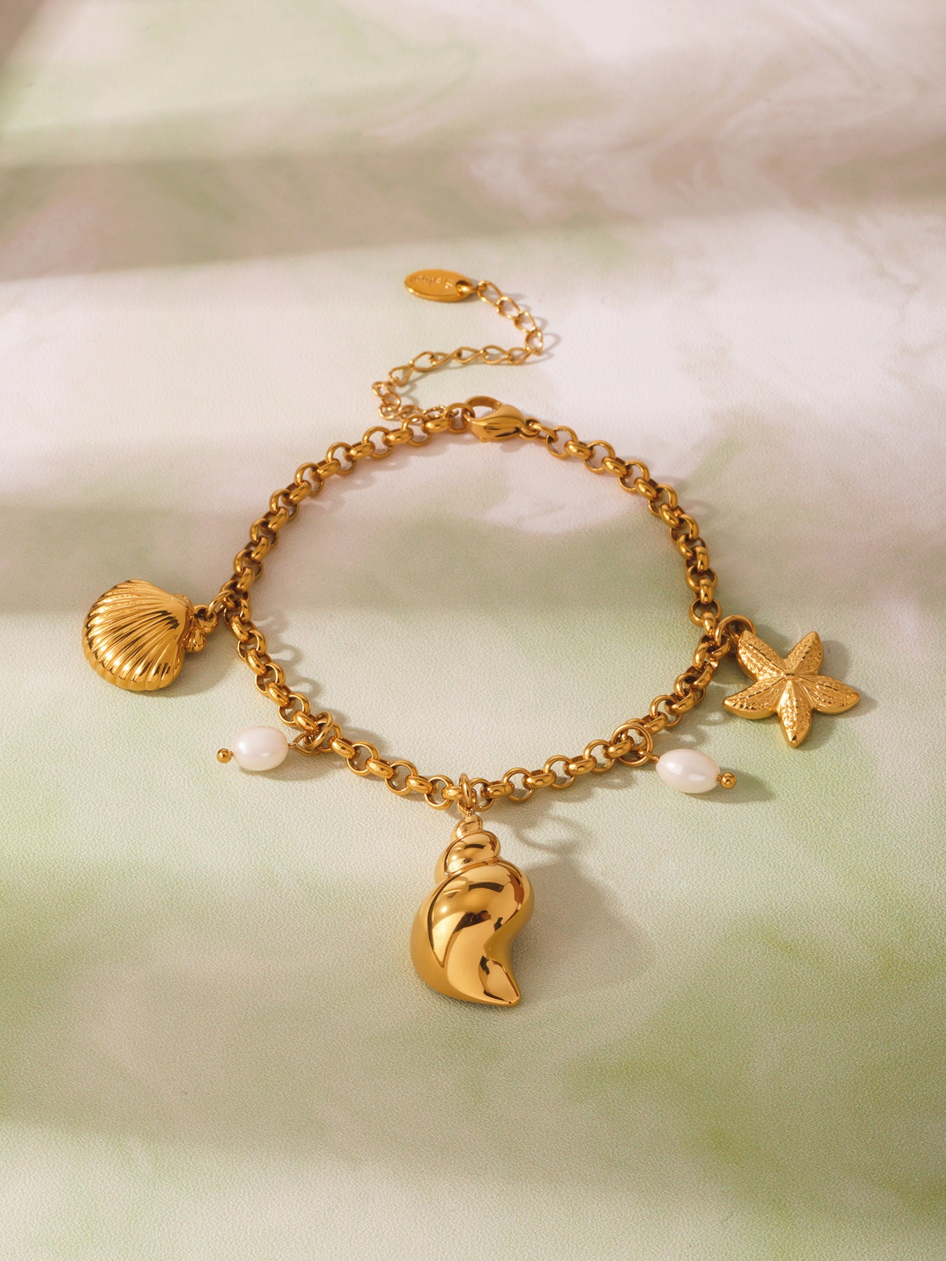 Studio flat lay of conch shell starfish and freshwater pearl charm anklet, 316L stainless steel 18K PVD gold finish