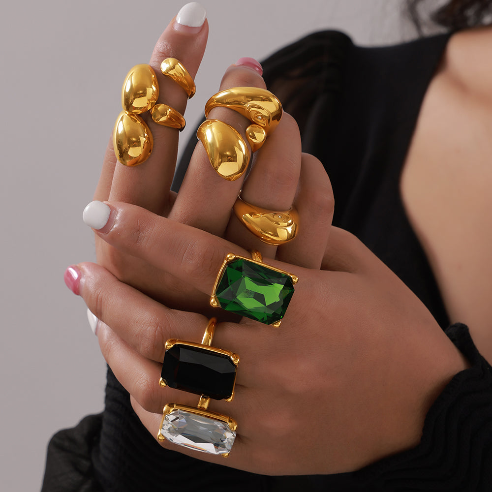 Close-up of hands wearing rectangular stone cocktail rings alongside rounded gold-tone sculptural rings