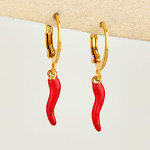 Pair of gold huggie earrings with bright red chili pepper charms displayed on a light background