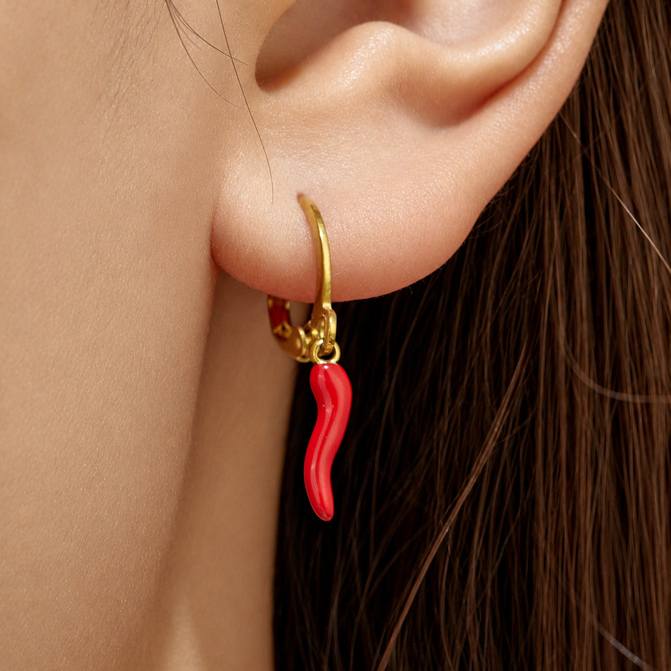 Model wearing gold huggie earrings with a slim red chili pepper charm