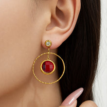 Model wearing red glass stone drop earrings in a gold-tone circular design