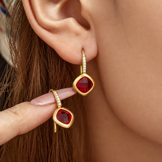Model wearing red glass stone drop earrings with polished gold-tone finish