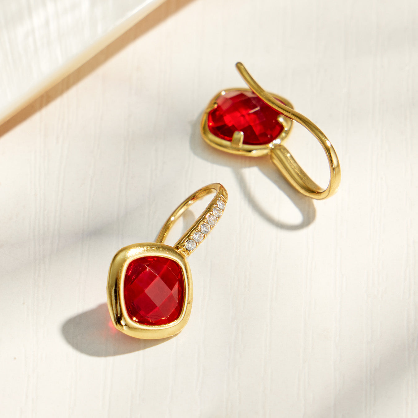 Red glass stone drop earrings showing faceted stone and gold-tone setting details